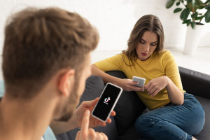 KYIV, UKRAINE - FEBRUARY 21, 2020: Selective focus of man using smartphone with tik tok app near girlfriend on couch