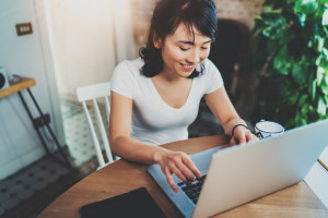 Top view of smiling Asian woman working on laptop while spending time at home.Concept young modern people using mobile devices.Blurred background,flares effect.